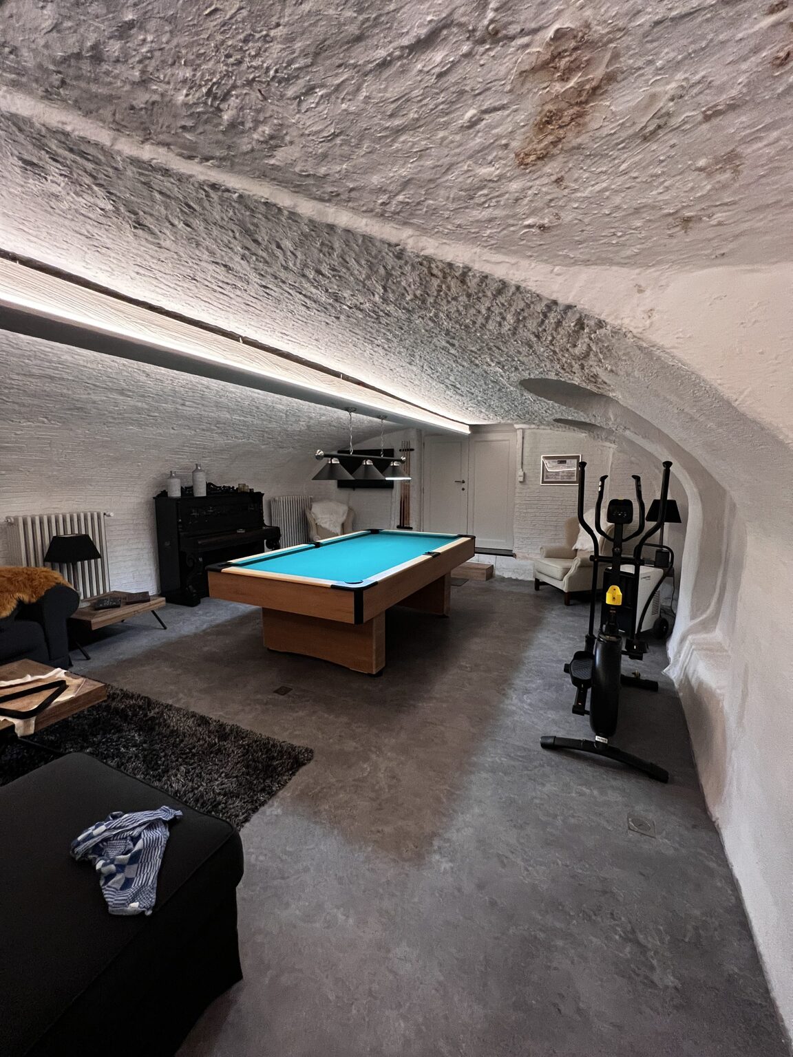 De afgewerkte mancave in Brugge met biljart, piano en fitnesstoestel onder een wit tongewelf